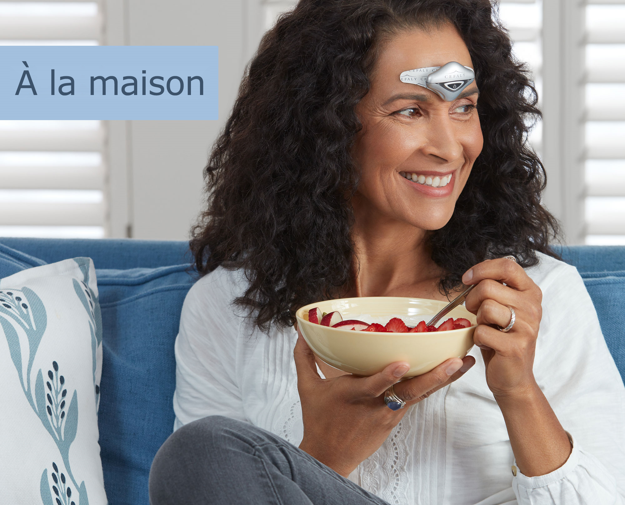 Femme en train de manger sur son canapé tout en utilisant son appareil CEFALY pour prévenir et traiter ses migraines.